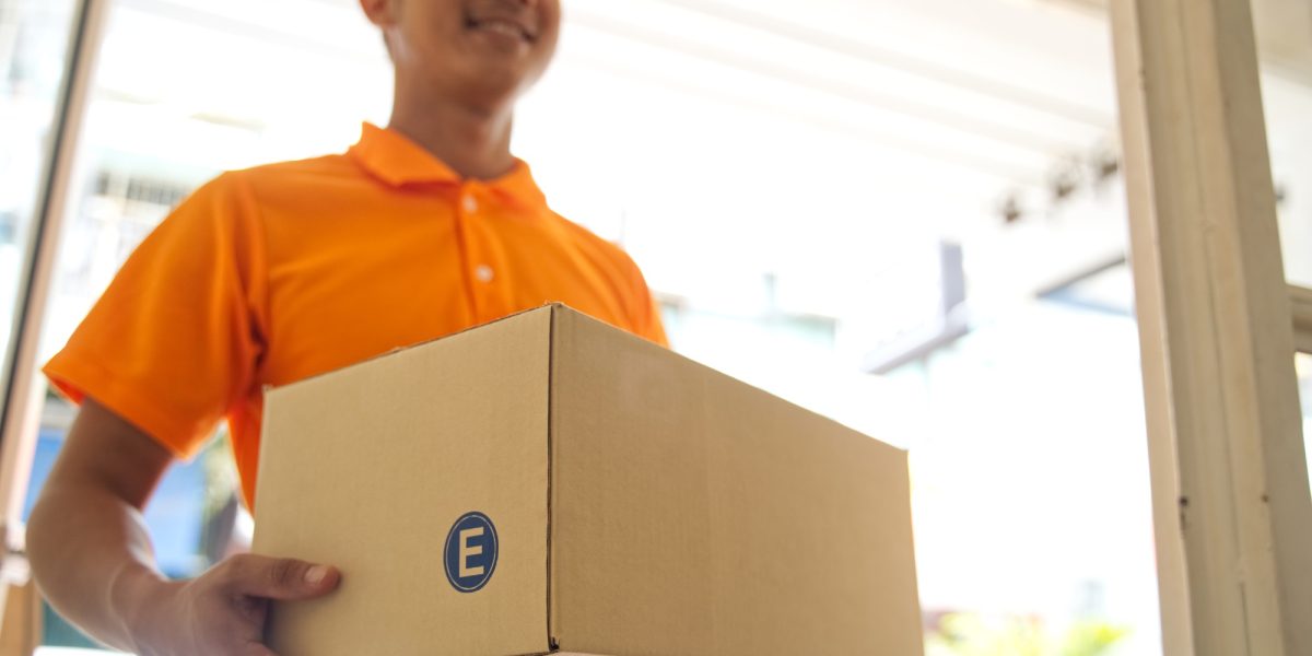 Delivery smiling Asian man in orange uniform and cap holding medium size of post box at the door.